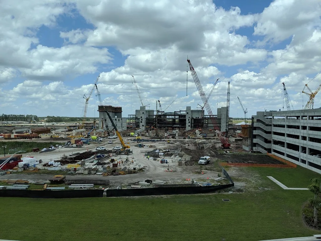 Crawler cranes, a yellow rough-terrain crane and tower cranes stand over a terminal under construction at Orlando International Airport in Orlando, Florida, with a parking garage at right.