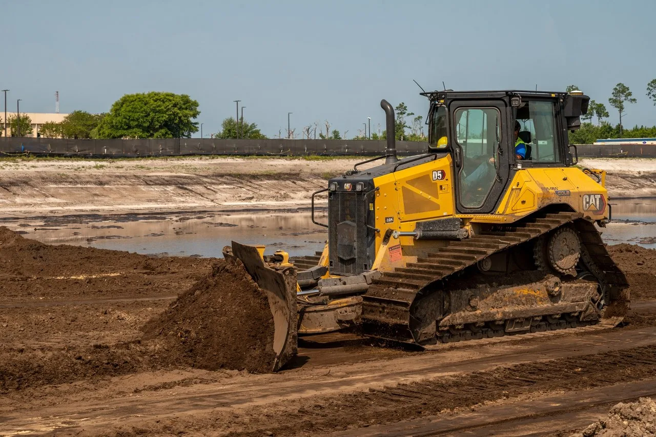 A yellow Cat D5 bulldozer pushes dark soil across a construction site at Tyndall Air Force Base, Florida, with the operator in the cab.