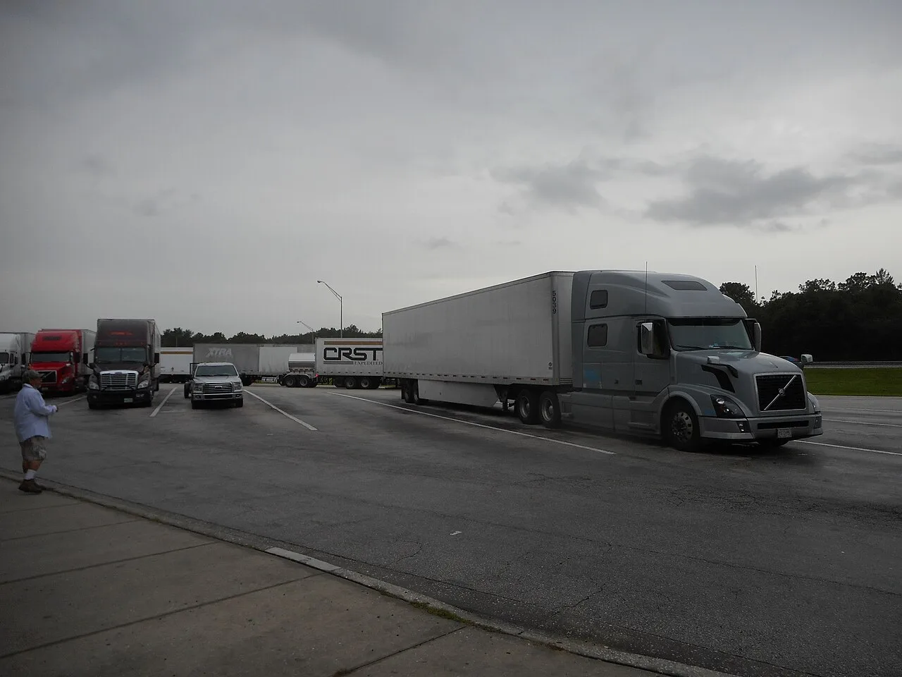 A gray Volvo semi truck and trailer parked in the truck lot of the northbound Interstate 75 rest area in Marion County, just south of Ocala, Florida, with more trucks and trailers behind it.
